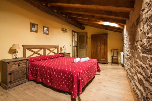 Amplio dormitorio rústico en casa rural de Ávila con ropa de cama de patrón rojo, vigas de madera, muro de piedra y estilo tradicional