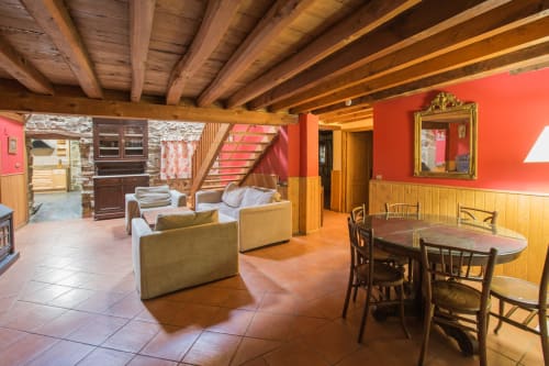 Amplia sala de estar en apartamento rural de Ávila con vigas de madera vista, paredes rojas, mesa de comedor y cómoda zona de descanso
