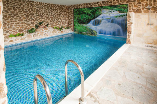 Piscina cubierta en Apartamentos Turísticos Ávila con mural de cascada, muros de piedra y barandillas metálicas