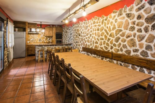 Rústico comedor en apartamento rural de Ávila con paredes de piedra, mesa de madera y zona de cocina