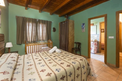 Amplio dormitorio en Apartamentos Turísticos Ávila con cama queen, vigas de madera, cuna, paredes verde menta y vistas a la montaña en zona rural