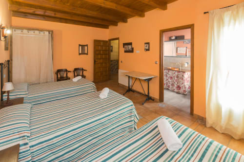 Dormitorio espacioso en Apartamentos Turísticos Ávila con ropa de cama a rayas, paredes naranjas, vigas de madera y vistas a la montaña