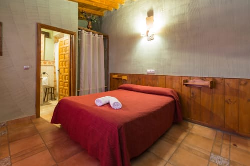 Dormitorio espacioso en Apartamentos Turísticos Ávila con ropa de cama roja, paredes de madera y baño en suite en Ávila, España.