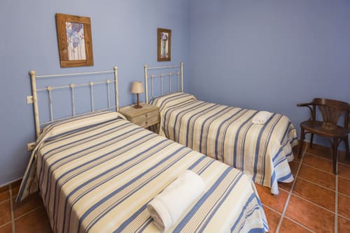 Dormitorio doble con ropa de cama a rayas en apartamento rural de Ávila, camas metálicas, mesilla de madera y suelos de parquet