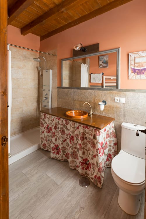 Baño en Apartamentos Turísticos Ávila con paredes naranjas, tocador de madera, lavamanos naranja y cabina de ducha