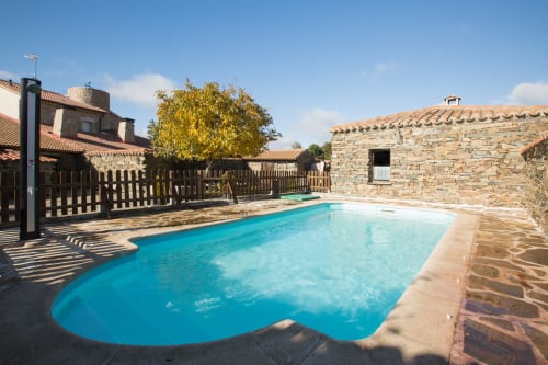 Bright blue swimming pool surrounded by stone buildings at Apartamentos Turísticos Ávila in Spain