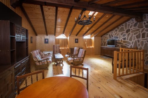 Rustic wooden loft interior at Apartamentos Turísticos Ávila with exposed beams, stone wall, comfortable seating, and wooden