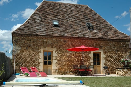 Maison en pierre du gîte Le Lapin sur le Toit avec transats rouges, parasol et piscine à Rouffignac, France