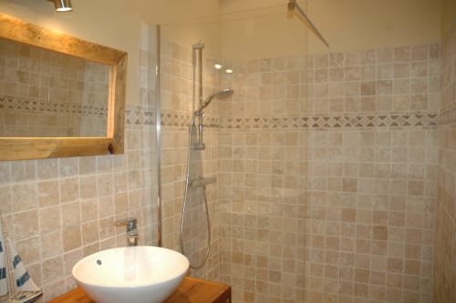 Salle de bain moderne du gîte Le Lapin sur le Toit avec vasque ronde, douche ouverte, carrelage beige et miroir en bois