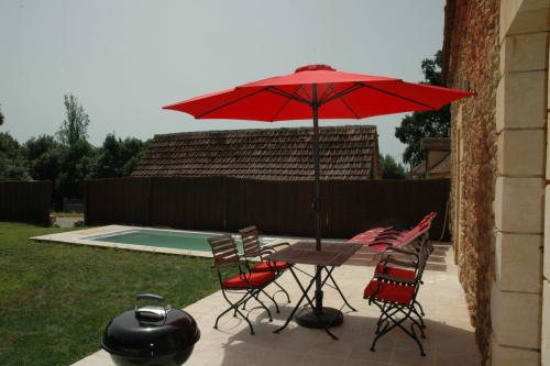 Terrasse au bord de la piscine du gîte Le Lapin sur le Toit avec parasol rouge, chaises longues et gril noir