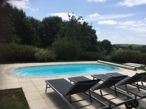 Piscine ovale aux eaux turquoise, transats noirs sur terrasse en pierre, verdure luxuriante au Lapin sur le Toit