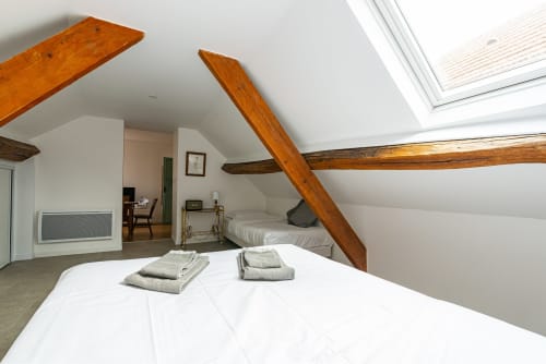 Bright attic bedroom at La Maison George with exposed wooden beams, white bedding, skylight, and rustic charm in Flavigny sur