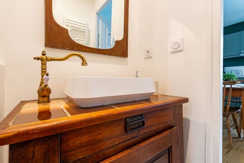 Elegant bathroom vanity at La Maison George with wooden basin cabinet, brass faucet, and framed mirror in Flavigny sur