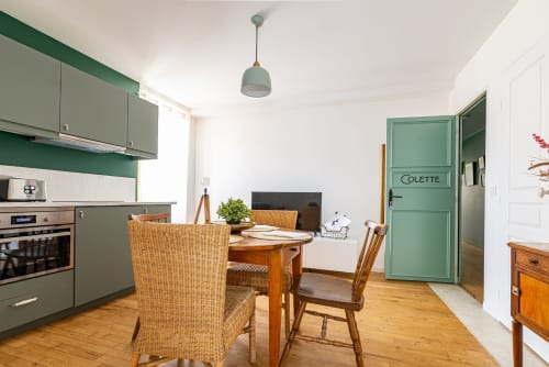 Logis Colette apartment at La Maison George: kitchen with green cabinetry, dining area with wooden table and wicker chairs,