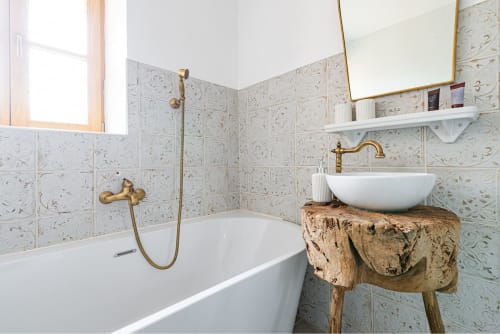 Rustic bathroom at La Maison George with patterned tile walls, vintage brass fixtures, white vessel sink on wooden stump