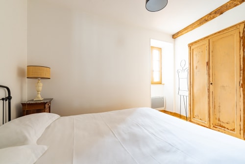 Bright bedroom at La Maison George with white bedding, wooden wardrobe, rustic beams, and natural light in