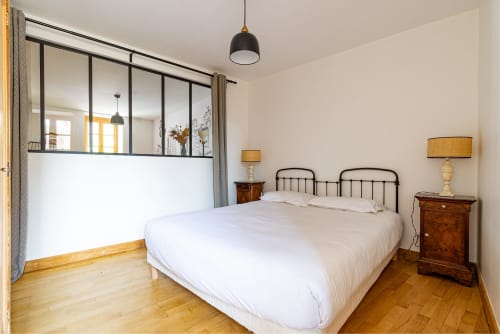 Modern bedroom at La Maison George in Flavigny sur Ozerain with queen bed, glass partition, wooden floors, and brass lamps.