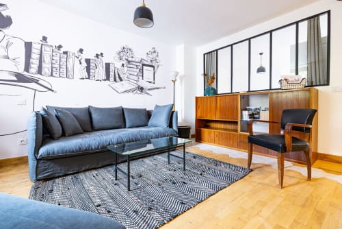 Modern living room at La Maison George hotel apartment in Flavigny sur Ozerain with blue sofa, wooden shelving, and