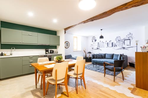 Appartement ouvert à La Maison George avec cuisine vert sauge, table à manger et salon avec canapé et fresque.