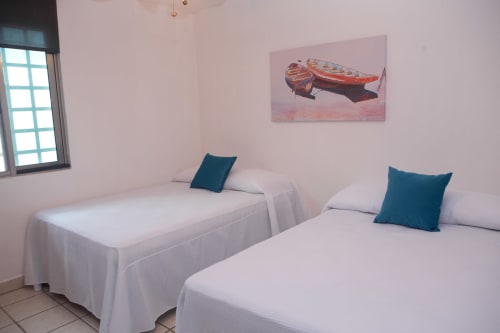 Habitación doble en Cozy House Downtown Cancun con camas blancas, almohadas color turquesa y cuadros de barcos en paredes rosadas
