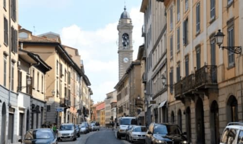 Rue historique du centre-ville de Bergame avec beffroi, voitures garées et architecture italienne traditionnelle