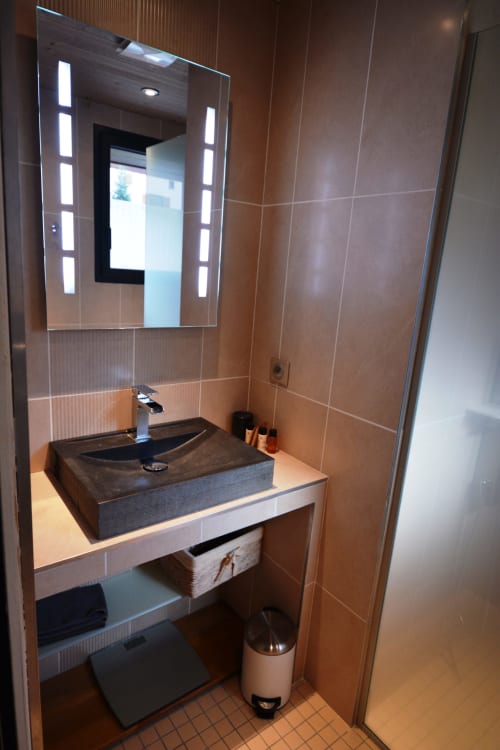 Salle de bains moderne à la Résidence Le Pacha, appartement de luxe à Courchevel, avec vasque en pierre sombre, miroir éclairant et
