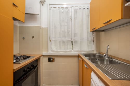 Cucina luminosa con mobili gialli, fornello a gas e finestra dell'hotel Re di Roma a Roma
