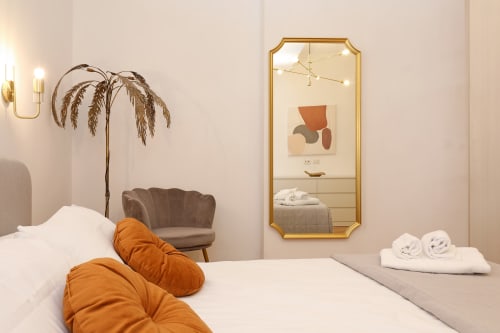 Camera moderna dell'Hotel Re di Roma a Roma con letto bianco, cuscini arancioni, specchio con cornice dorata e arredamento minimalista