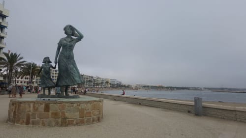 Statue de bronze d'une femme et d'un enfant sur la promenade de plage avec la Méditerranée et les bâtiments côtiers