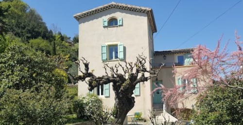 Le Mas de Trépeloup, gîte à Alès avec tour en pierre crème, volets turquoise, cerisier en fleur et jardins luxuriants
