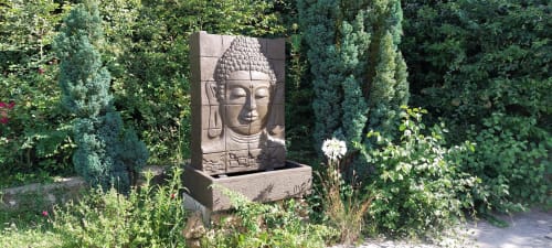 Sculpture de Bouddha en pierre entourée de verdure luxuriante au jardin Le Mas de Trépeloup, Alès, France