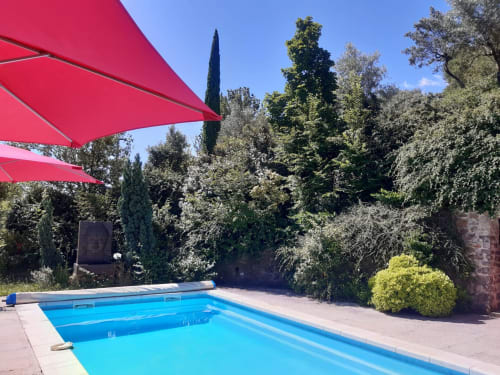 Piscine bleu vif avec voiles d'ombrage rouges au Mas de Trépeloup à Alès, entourée de verdure luxuriante et de cyprès