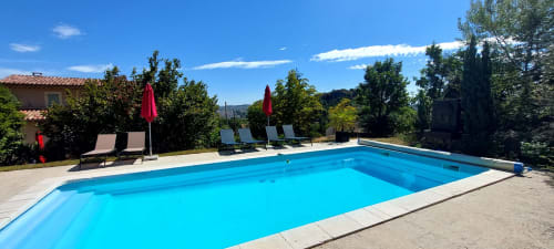Piscine bleu cristal du gîte Le Mas de Trépeloup à Alès, avec transats et parasols rouges