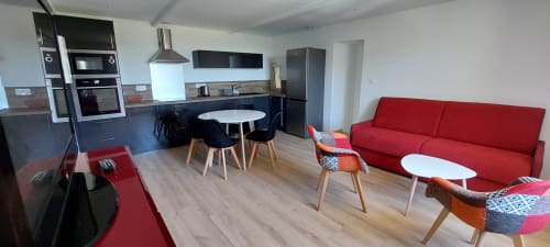 Espace de vie ouvert et moderne au gîte Le Mas de Trépeloup à Alès avec canapé rouge, table à manger et cuisine équipée