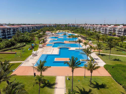 Vista aérea del Resort Mareazul con piscinas azul vibrante, palmeras y modernos departamentos en Playa del Carmen