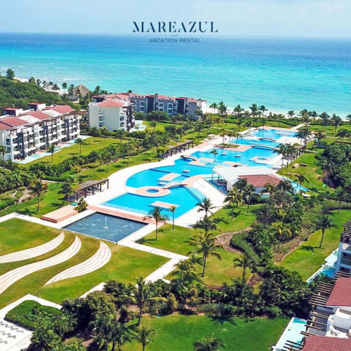 Vista aérea del Resort Mareazul con piscinas turquesas, edificios frente al mar y jardines tropicales en Playa del Carmen