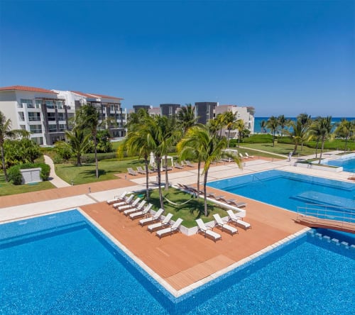 Área de piscina del Resort Mareazul frente al mar con tumbonas, palmeras y vista al océano en Playa del Carmen