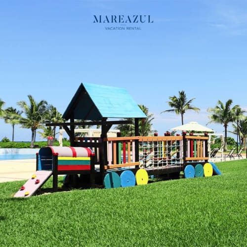 Colorido parque infantil con equipamiento en forma de tren sobre césped verde en Mareazul Resort Frente al Mar, Playa del Carmen