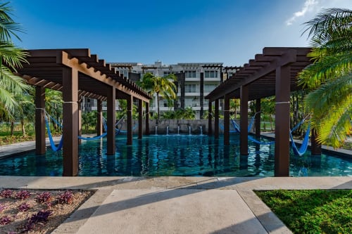 Piscina infinita de aguas turquesas del Resort Mareazul frente al mar, con pérgolas de madera oscura y palmeras en Playa del Carmen