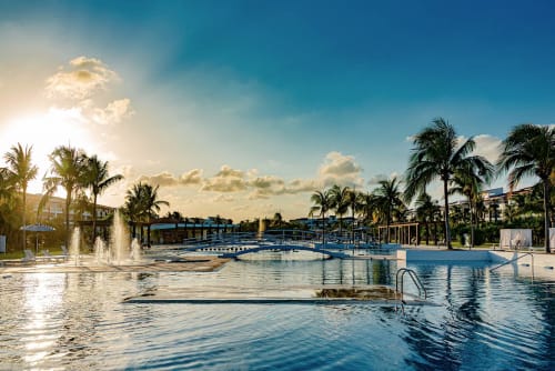 Piscina frente al mar del Resort Mareazul con fuentes, palmeras y vistas al océano en Playa del Carmen