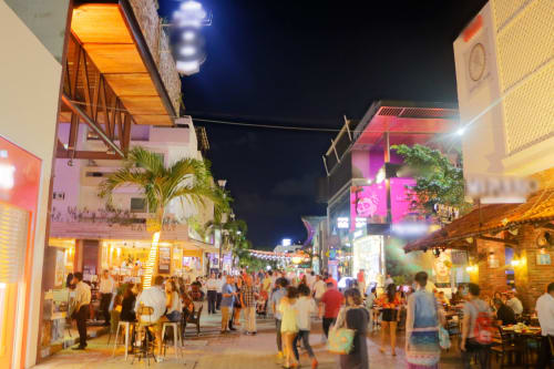 Animada escena nocturna en Playa del Carmen con coloridas tiendas, multitudes y palmeras tropicales a lo largo de la calle