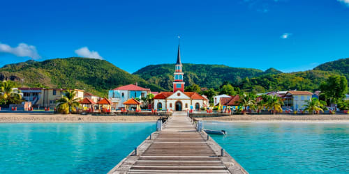 Débarcadère en bois s'étendant dans les eaux turquoise vers un village balnéaire coloré avec église, Les Anses d'Arlet, Martinique