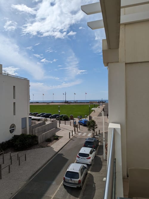 Vue depuis le balcon de l'appartement Côte et Dune à Biscarrosse Plage surplombant l'océan, pelouse verte, drapeaux et voitures garées
