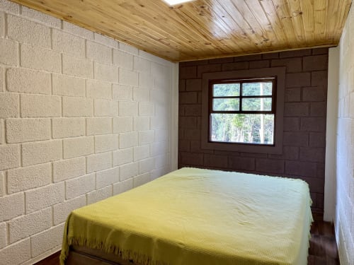 Quarto aconchegante na Paraíso nas Montanhas com cama amarela, paredes de tijolos, teto de madeira e vista da floresta montanhosa
