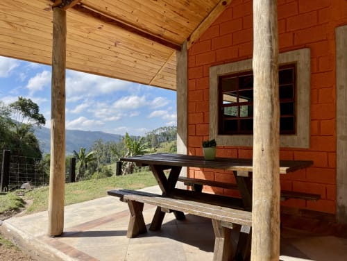 Varanda da villa na montanha do Paraíso nas Montanhas com móveis rústicos de madeira, paredes de tijolos vermelhos e vista panorâmica de Campos do Jordão