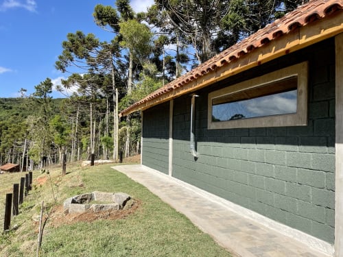 Villa na montanha em Paraíso nas Montanhas, Campos do Jordão, com telhado em terracota, paredes de pedra verde e vista da floresta