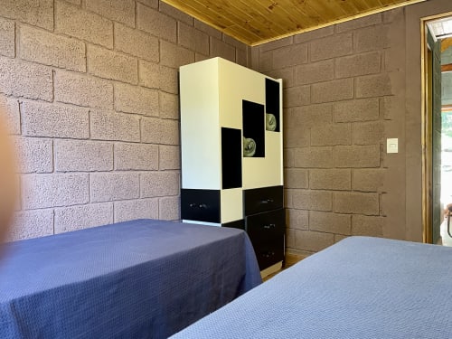 Quarto da villa na montanha em Paraíso nas Montanhas com duas camas, guarda-roupa moderno preto e branco, e paredes de tijolo.