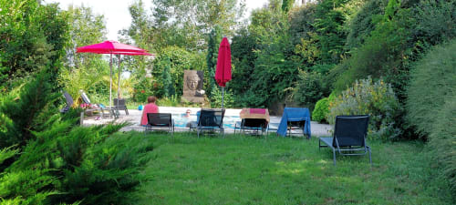 Espace de détente au jardin du Mas de Trépeloup à Alès avec transats, parasols rouges et verdure luxuriante