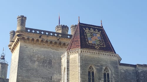 Tour de château médiéval en pierre avec tourelles et toit aux tuiles décoratives, hébergement à Alès France