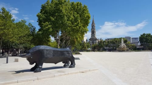 Sculpture de taureau noir sur la place d'Alès avec église gothique et arbres verts sous un ciel bleu